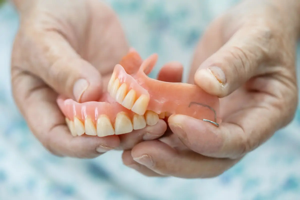 Hands holding a complete denture showing upper and lower teeth for patient education.