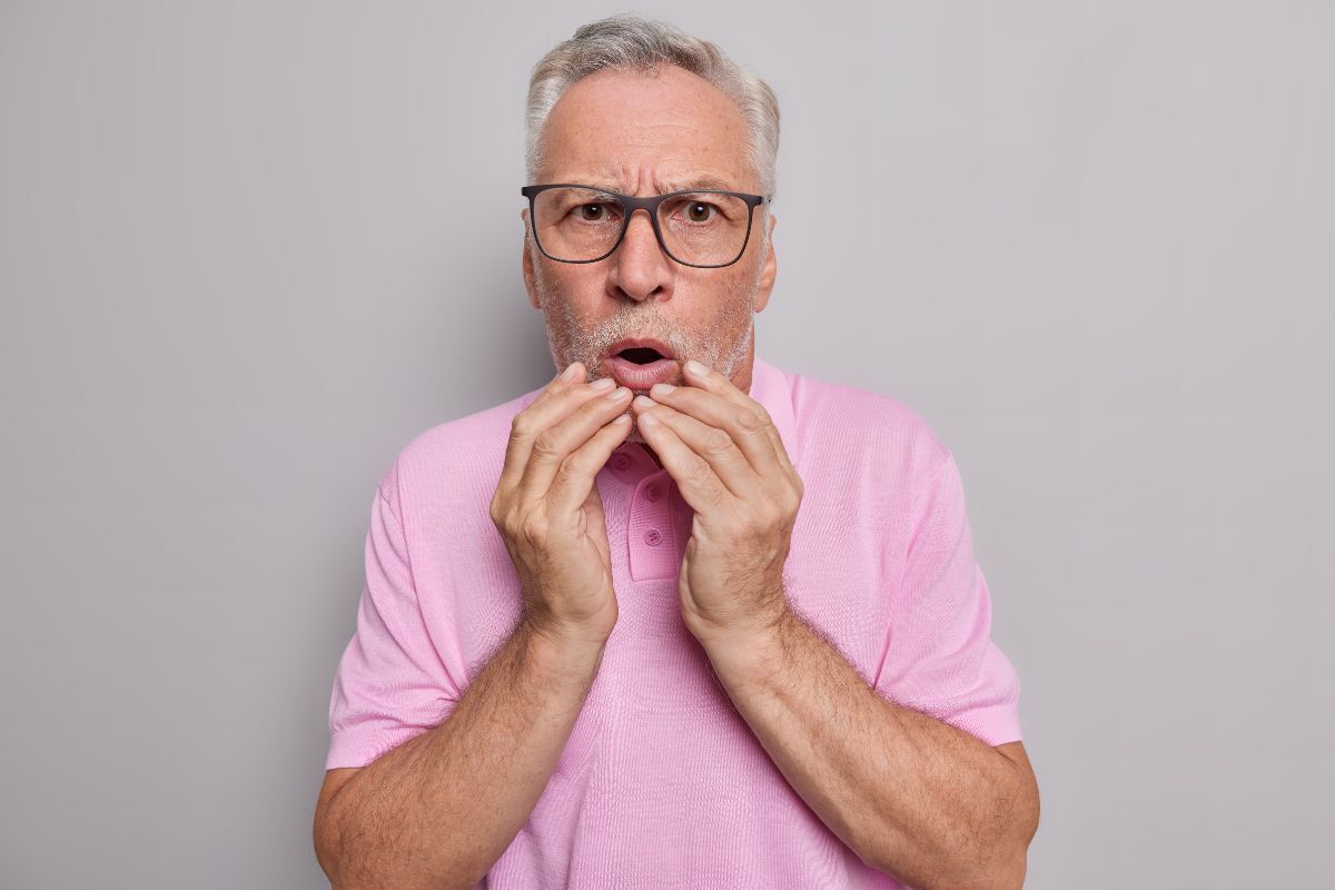 Older man with glasses experiencing dental pain, holding his cheek in discomfort.